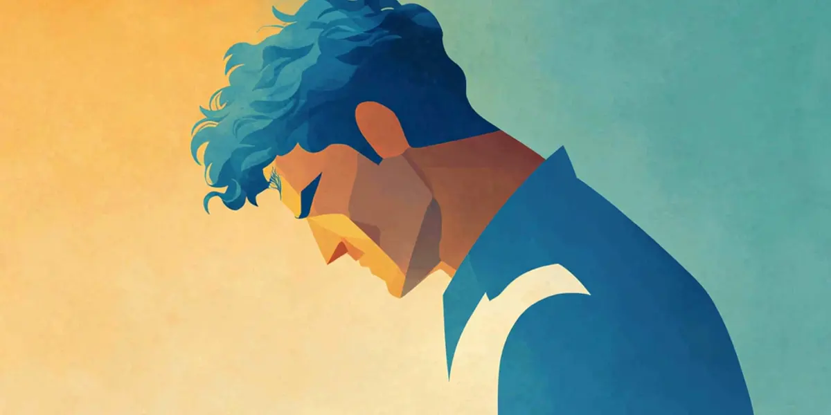 A man in a blue shirt bows his head with a tense, downcast expression against a split warm-and-cool background.